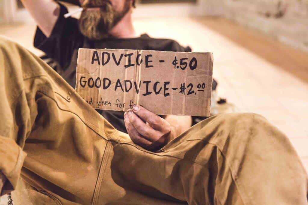 Street beggar with sign saying advice costs $0.50 and good advice costs $2.00